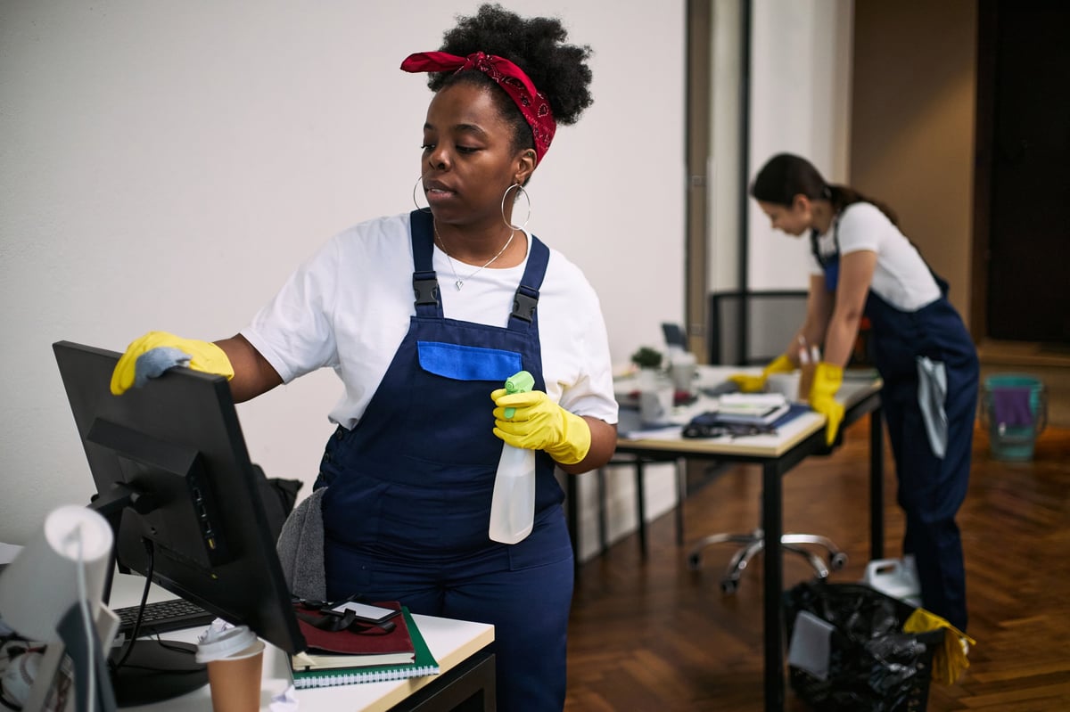 Commercial cleaning staff wiping down monitors and desks in a modern office